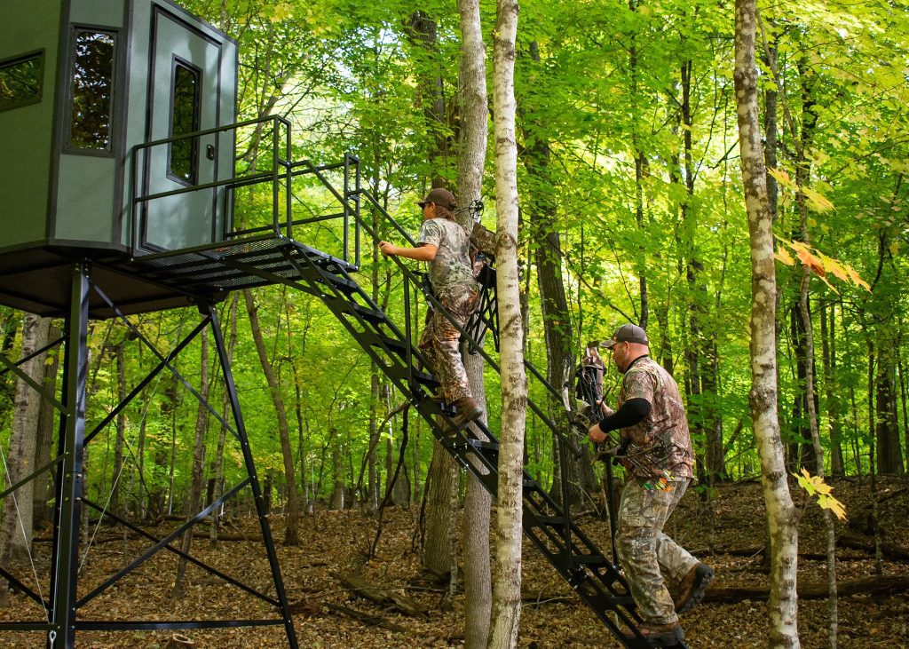 Two hunters climbing up stairs of elevated ambush blind