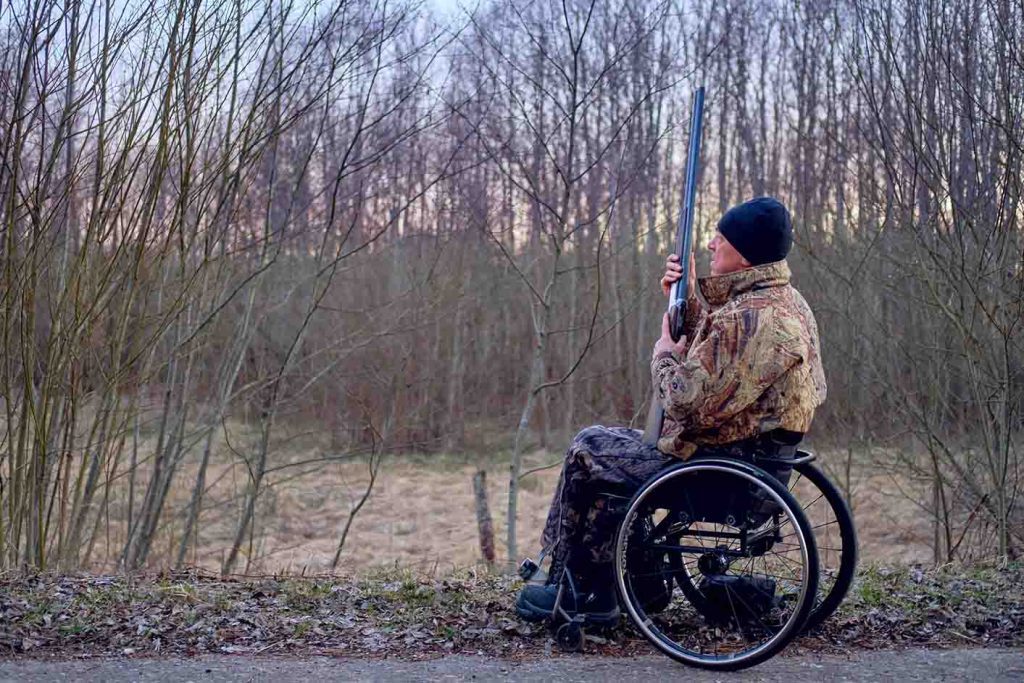 camouflage wheelchair hunter in forest with gun