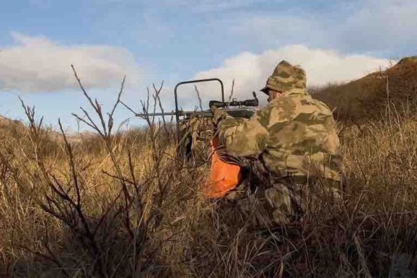 Hunter sitting in field aiming firearm