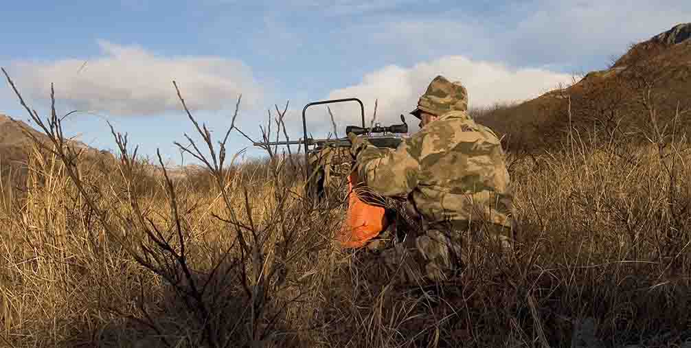 Hunter sitting in field aiming firearm